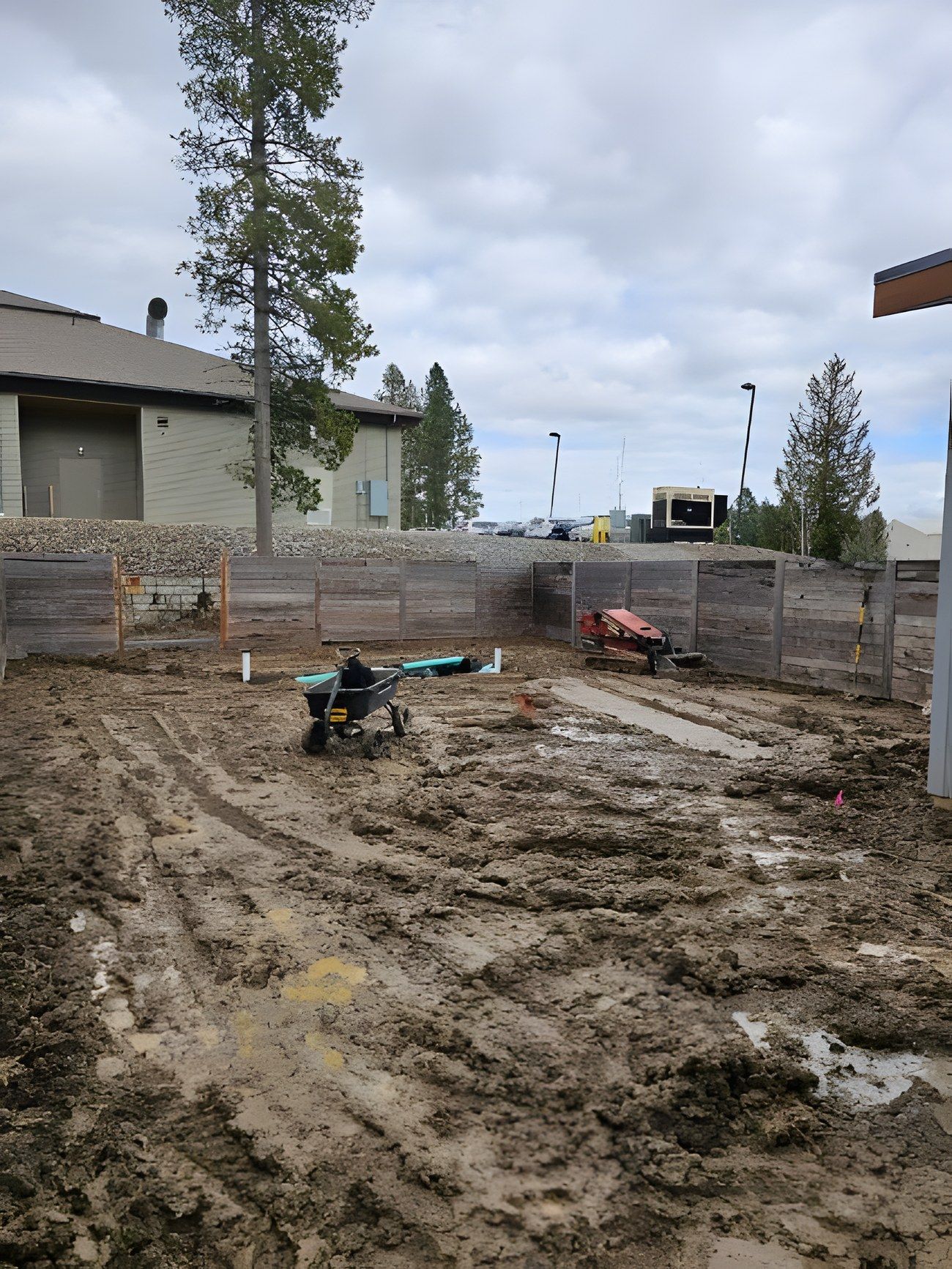 Muddy fenced backyard being regraded, with tools and a wheelbarrow