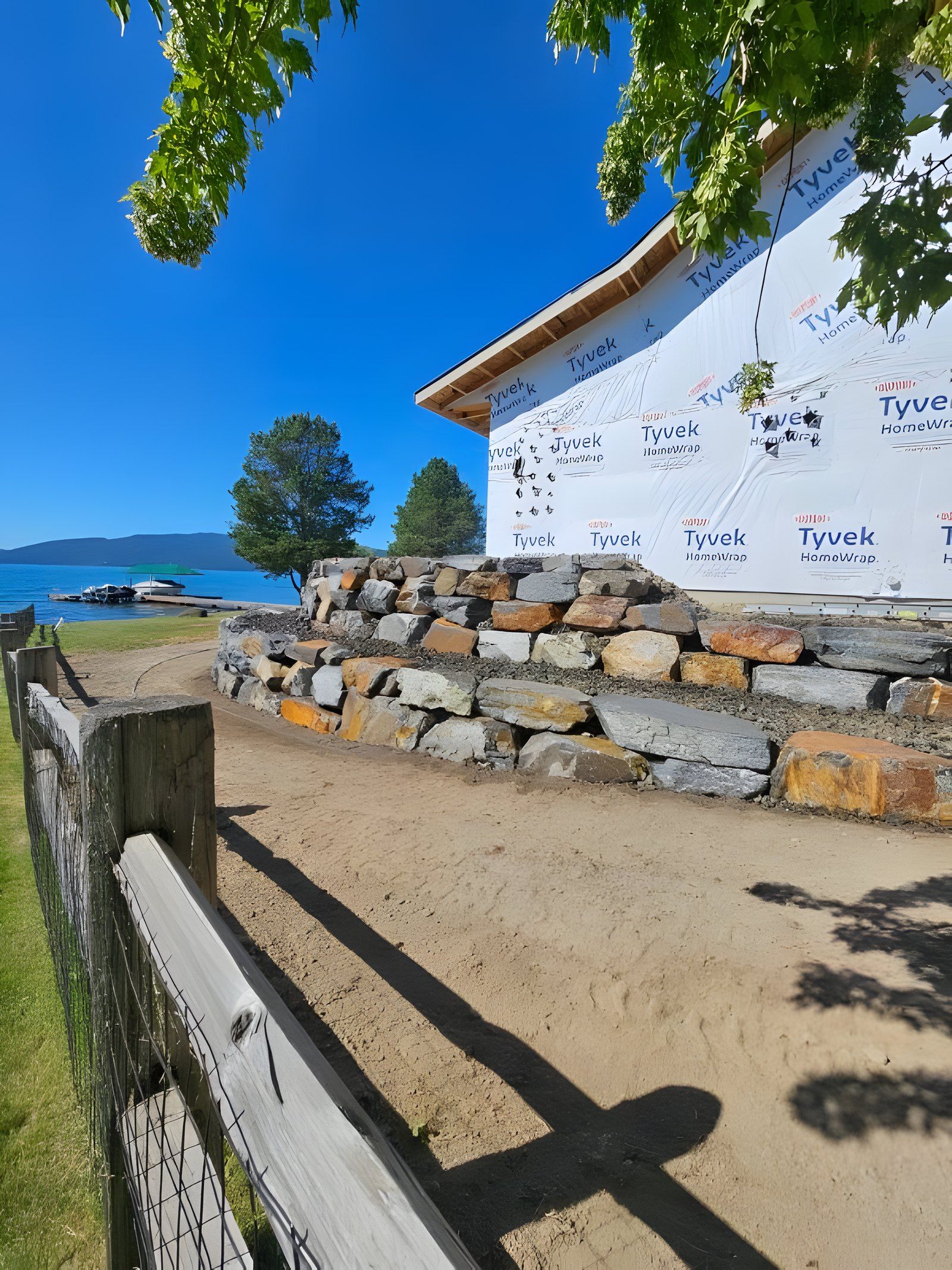Boulder retaining wall seen from a wood rail fence, with the lake and a dock in the distance
