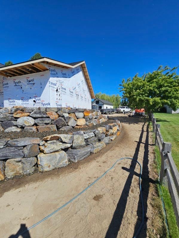 Boulder wall running along a graded dirt side yard next to a rail fence
