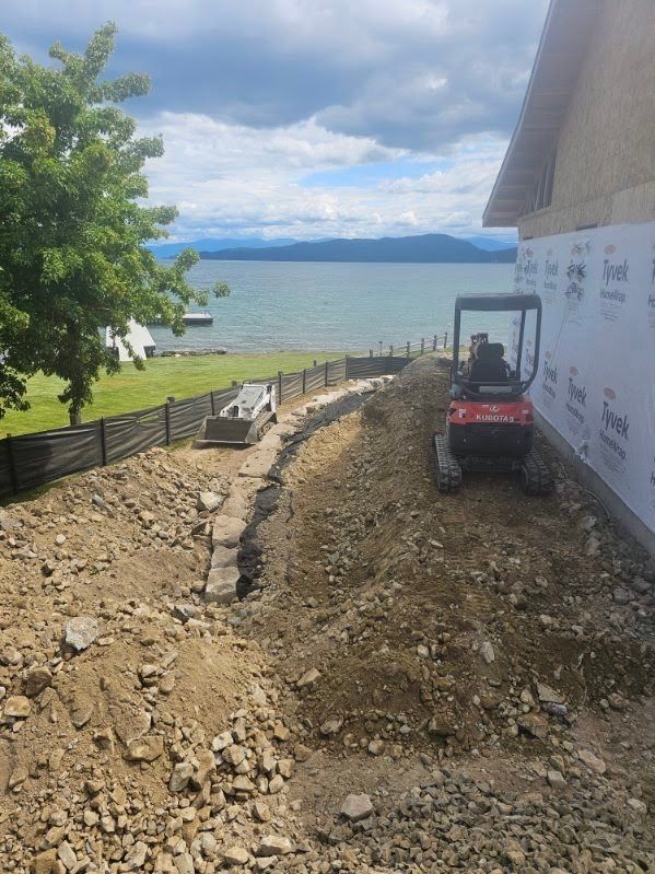 Mini excavator digging along the side of a house with the lake in the background