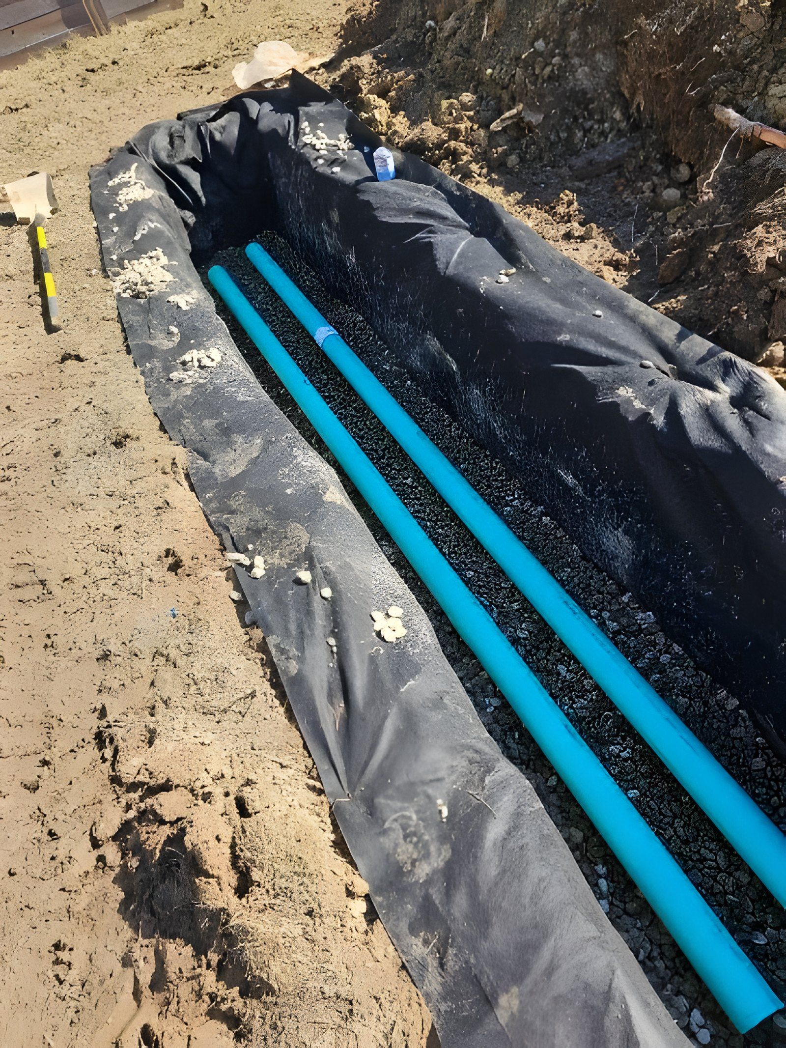 Two runs of green pipe laid on gravel in a trench lined with black fabric