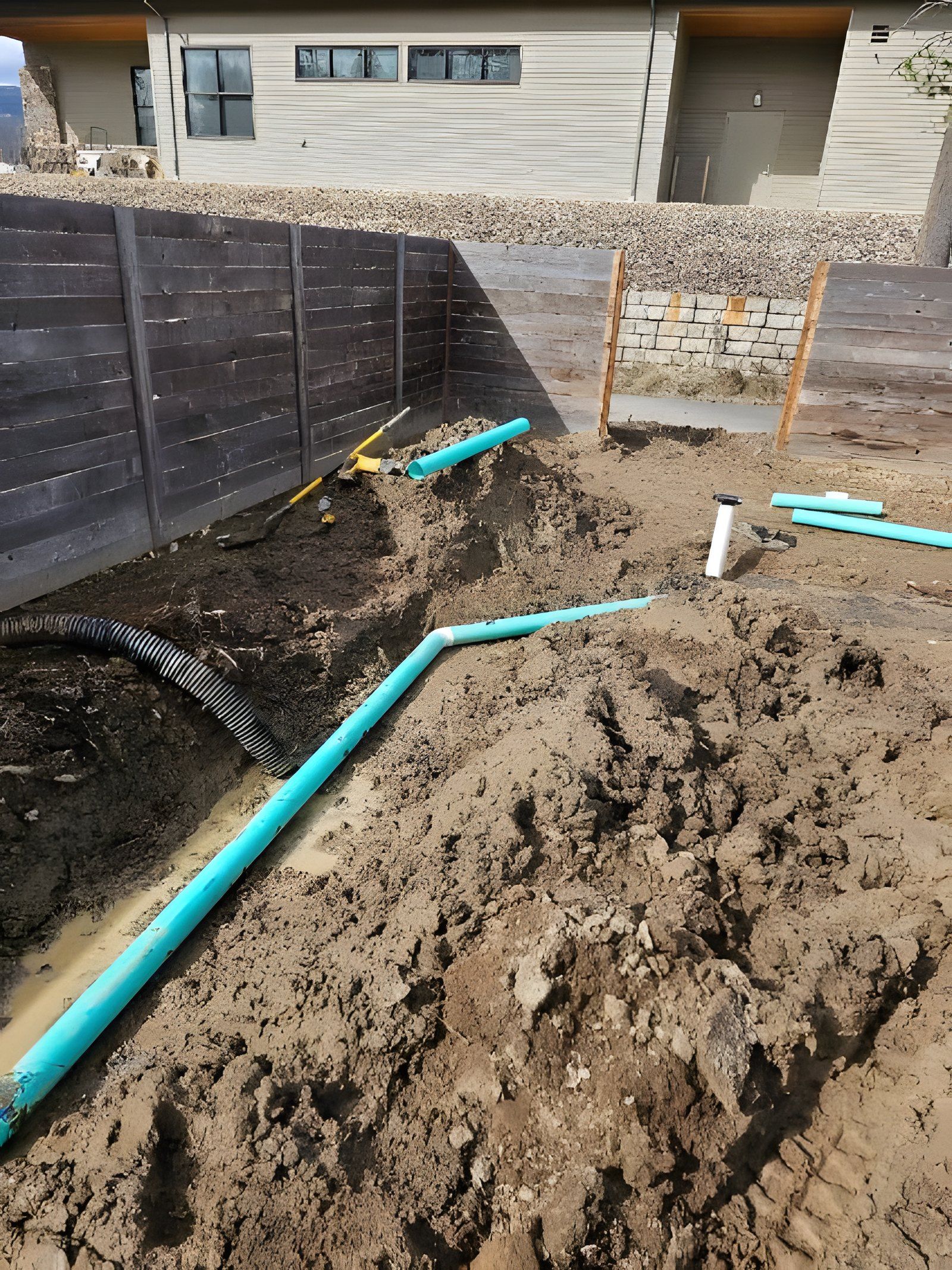 Green drain pipe running through a dug-out backyard along a wood fence