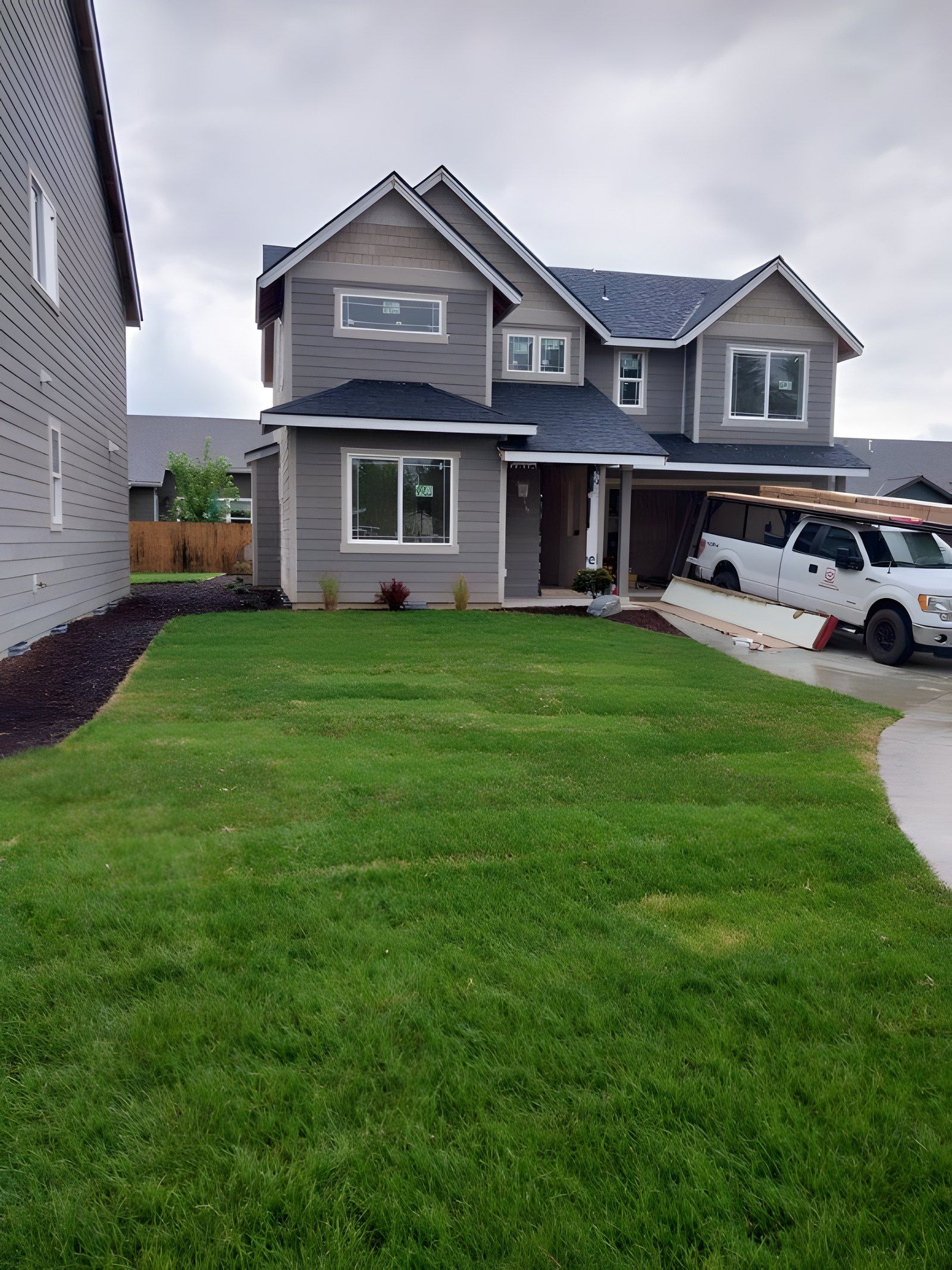 Green sod front lawn and mulch beds in front of a two-story gray house