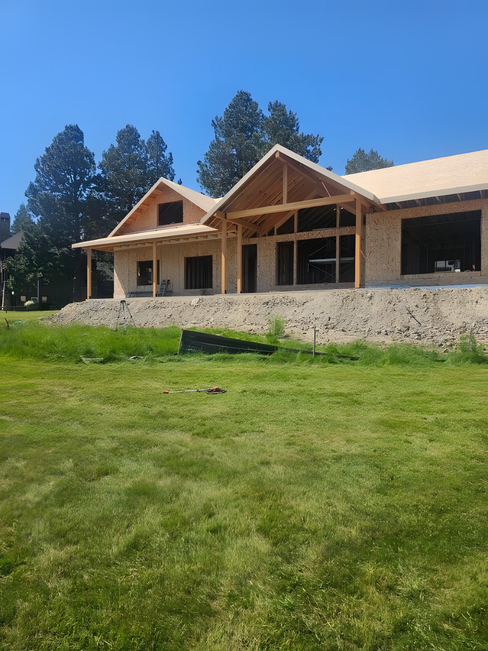 Framed house with a timber porch and a bare dirt slope along the front, before the curved boulder wall went in