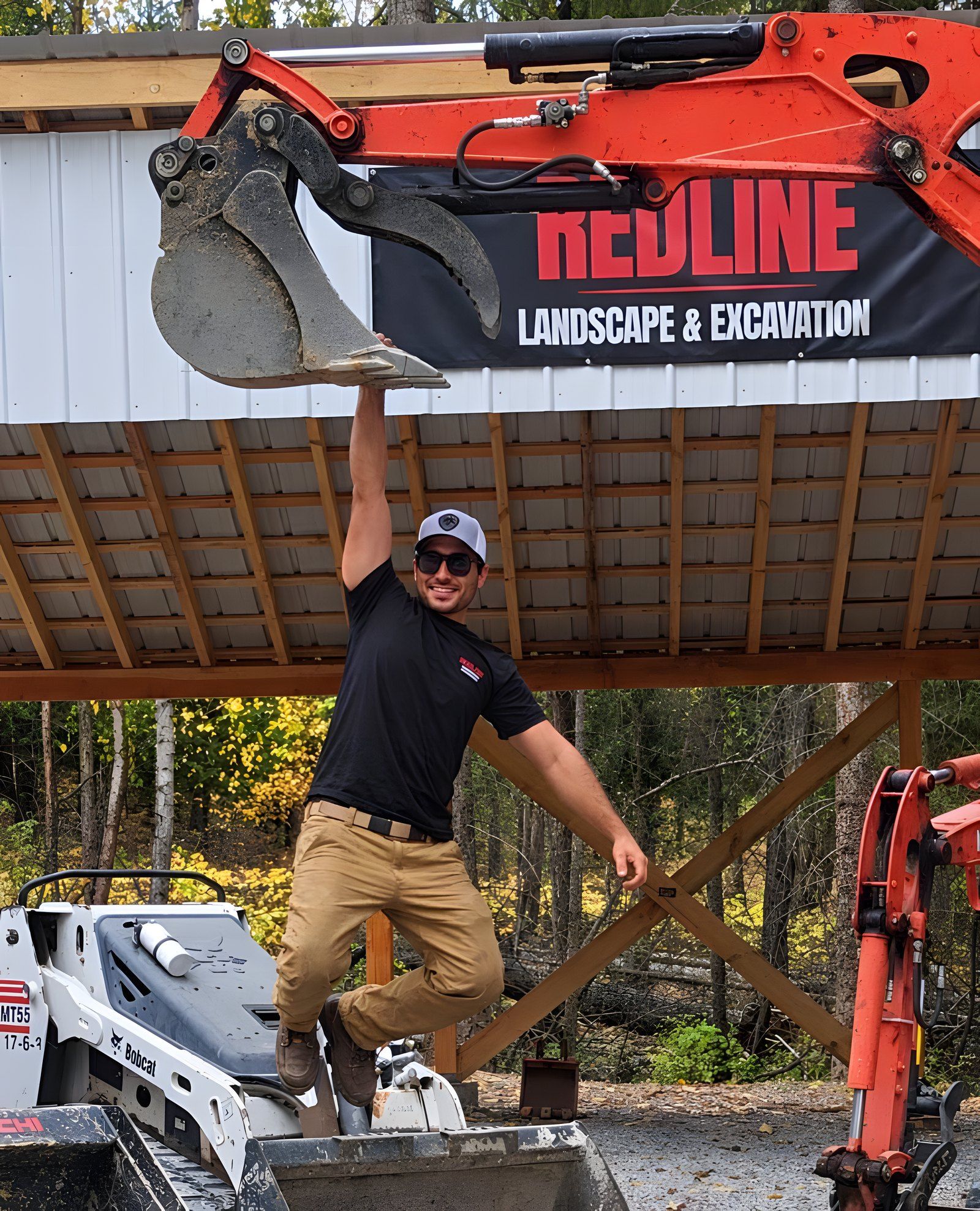 Peter LaBarbera hanging from an excavator bucket under the Redline Landscape & Excavation banner