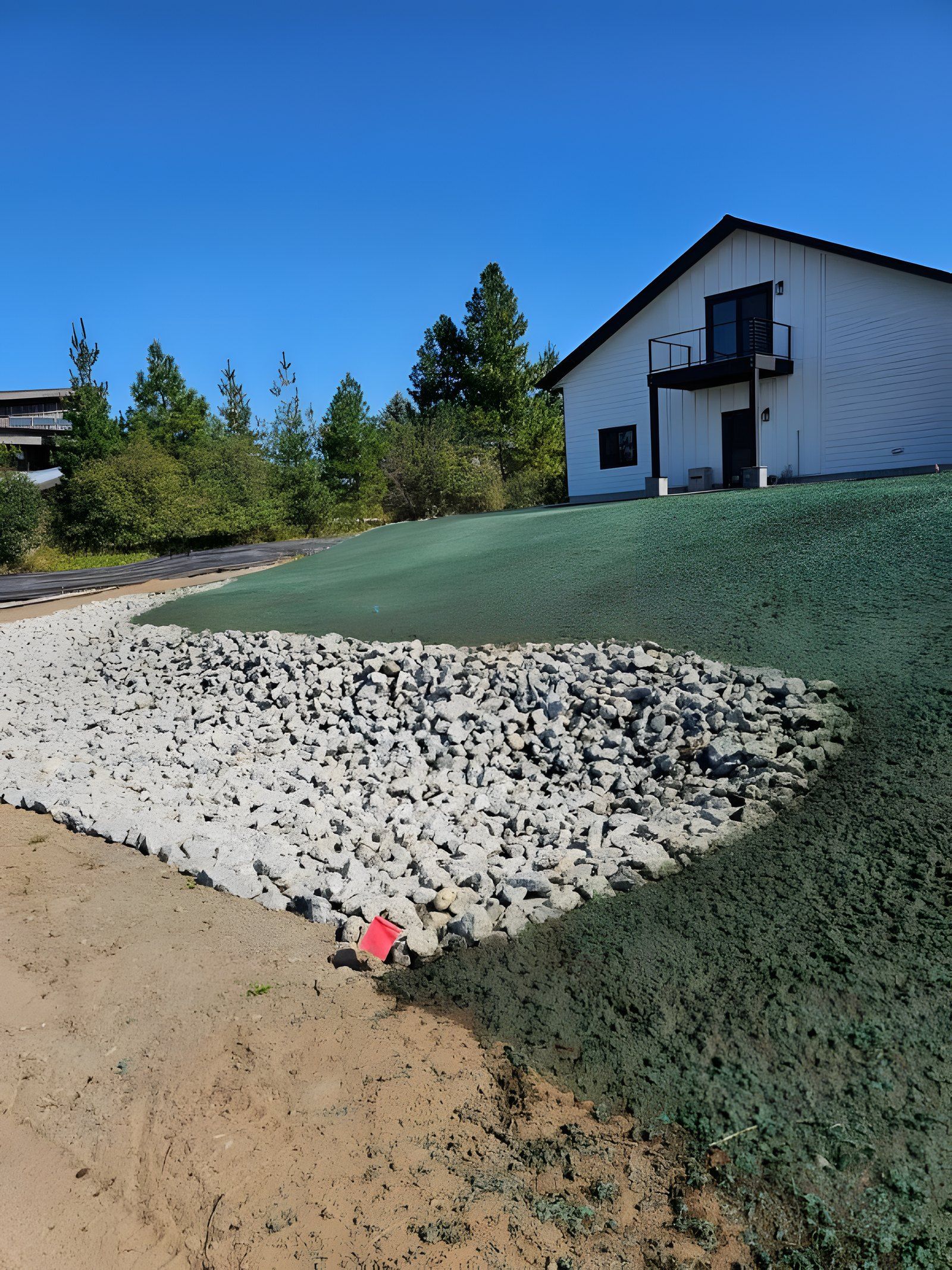 The same slope after work, with a band of rock and fresh green hydroseed below the house